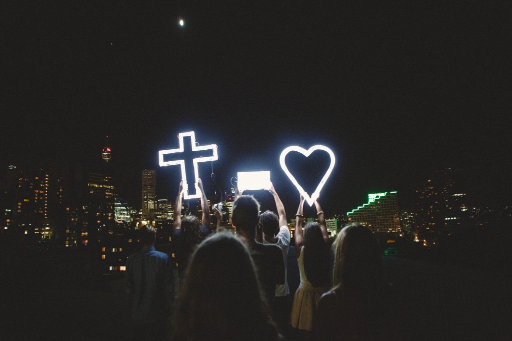 crowd of people at night holing a lighted cross and heart