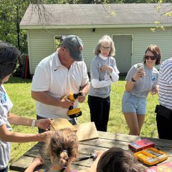 Adults helping children make a bird house on a picnic table